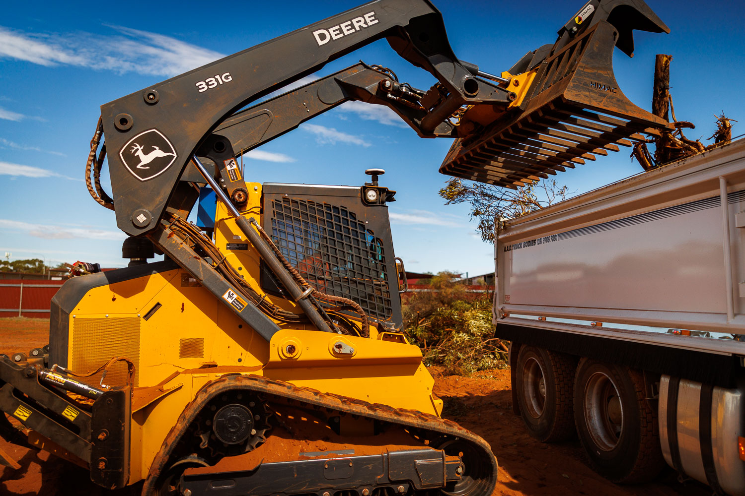 John Deere 331G loading vegetation debris into tipper
