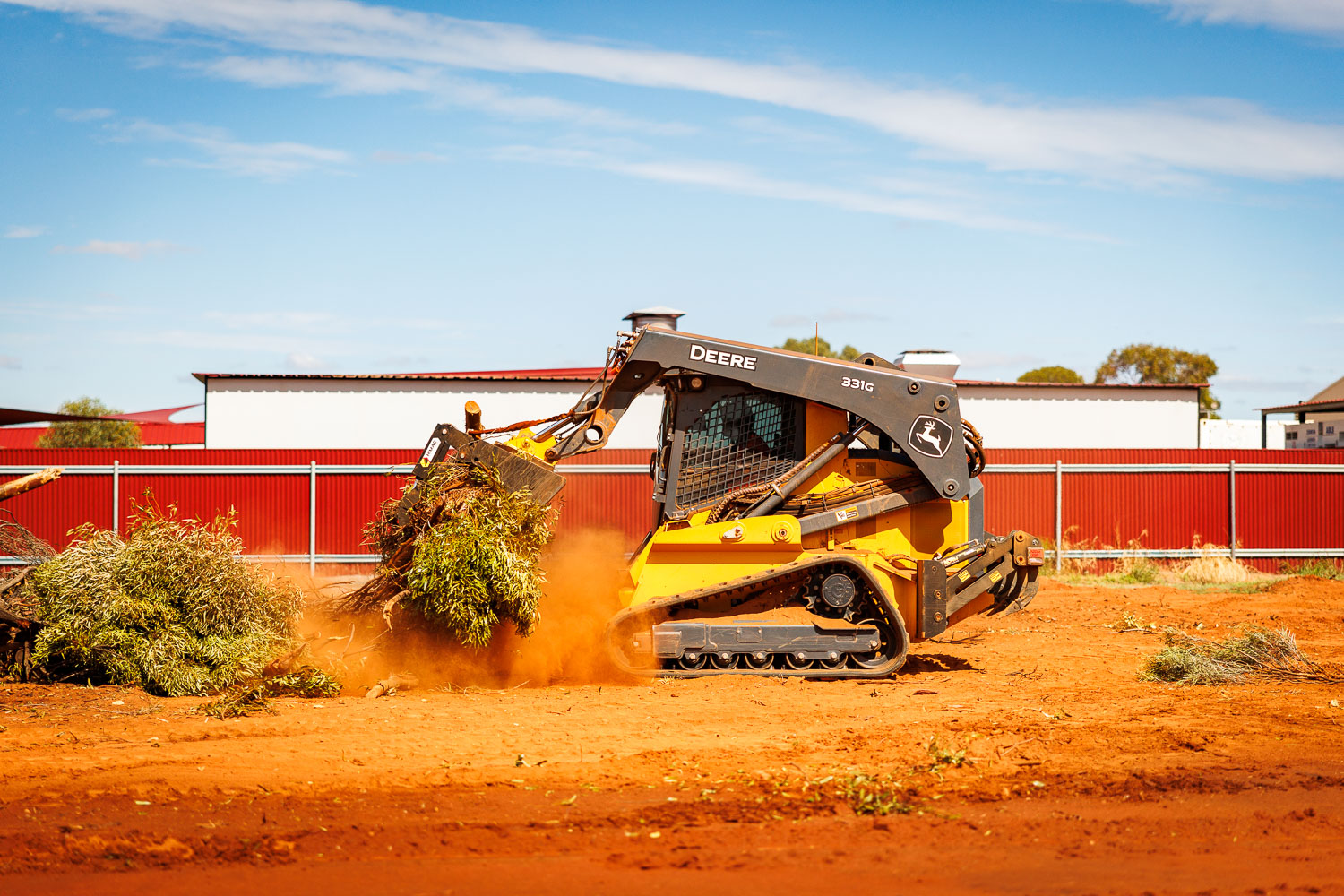 John Deere 331G CTL clearing vegetation and debris on site